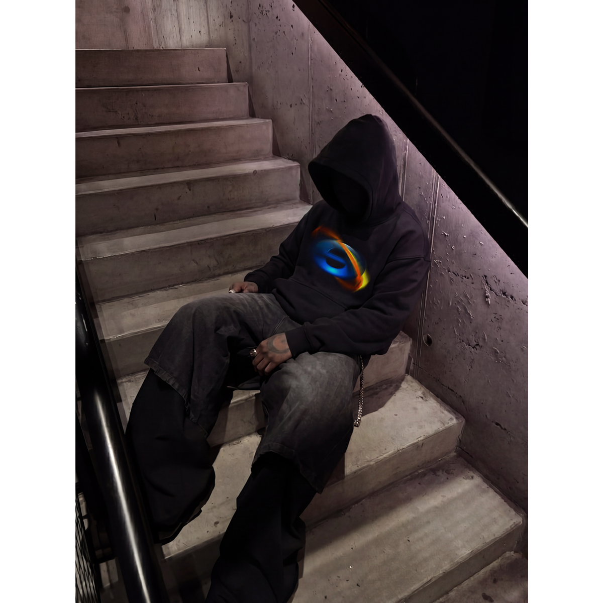Person wearing a black hoodie with a colorful logo sitting on concrete stairs.