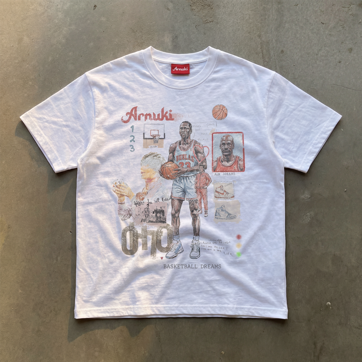 White t-shirt with basketball-themed graphics and text on a concrete surface